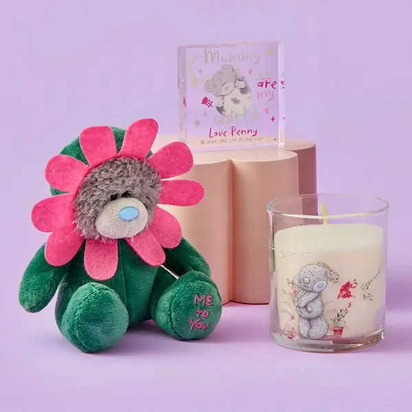 Plush flower‑costumed bear sitting beside a Me to You candle and a small personalised acrylic block, all arranged on a soft pastel background.